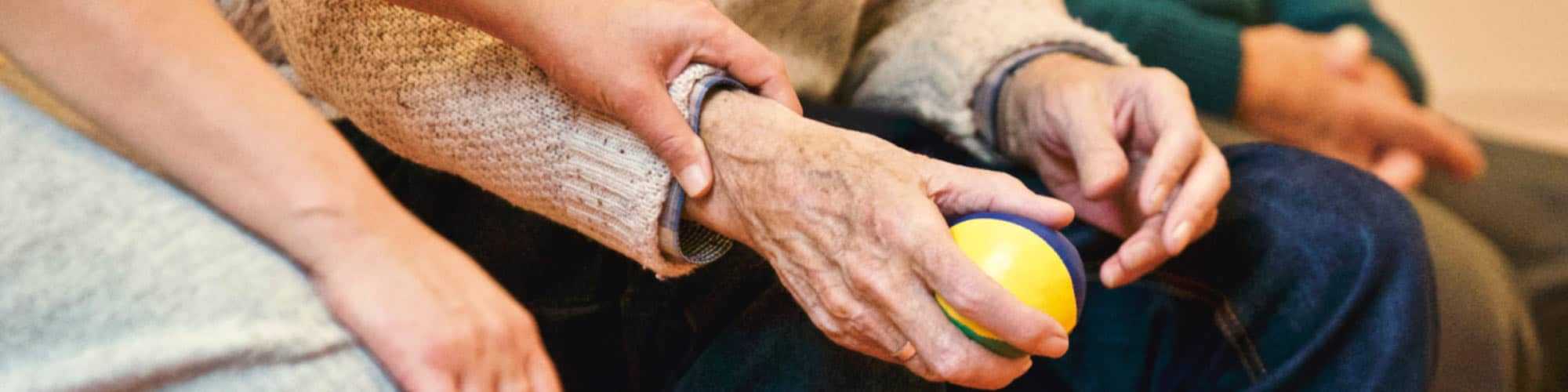 Elderly person holding a ball with caregiver assisting their wrist